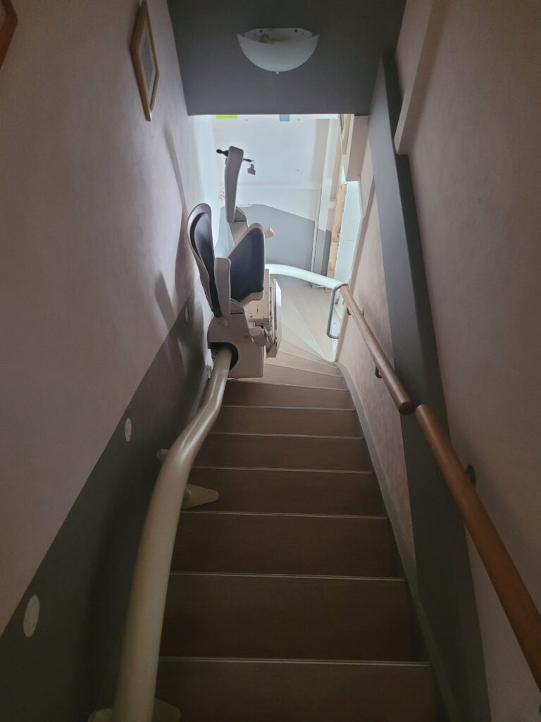 Vue plongeante sur monte-escalier installé dans escalier droit avec double rampe