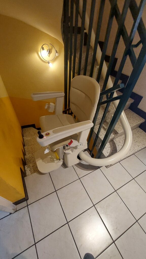 Monte-escalier avec siège beige en bas d'un escalier avec garde-corps métallique noir