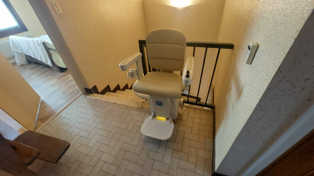 Monte-escalier avec siège beige en bas d'un escalier avec garde-corps métallique noir