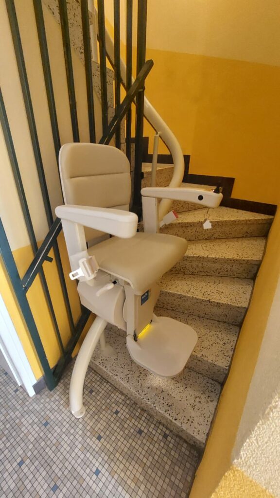 Monte-escalier avec siège beige en bas d'un escalier avec garde-corps métallique noir