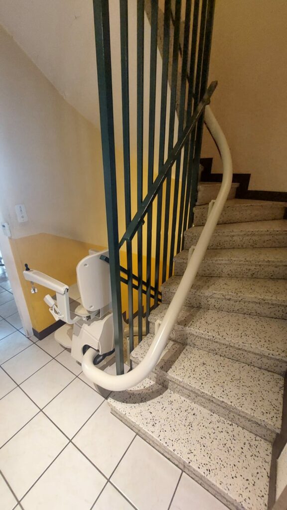 Monte-escalier avec siège beige en bas d'un escalier avec garde-corps métallique noir