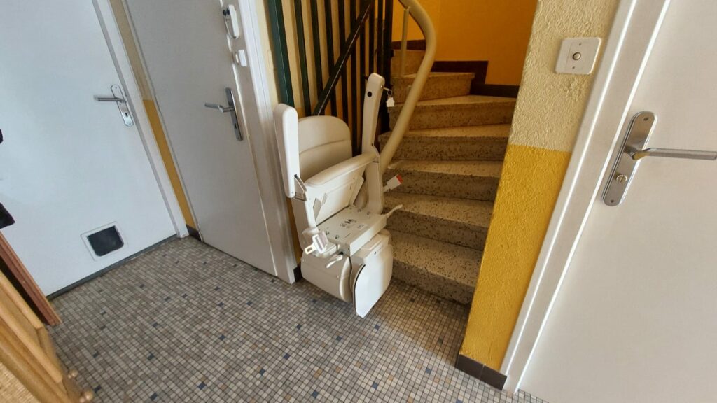 Monte-escalier avec siège beige en bas d'un escalier avec garde-corps métallique noir