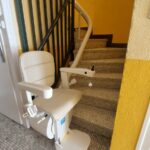 Monte-escalier avec siège beige en bas d'un escalier avec garde-corps métallique noir