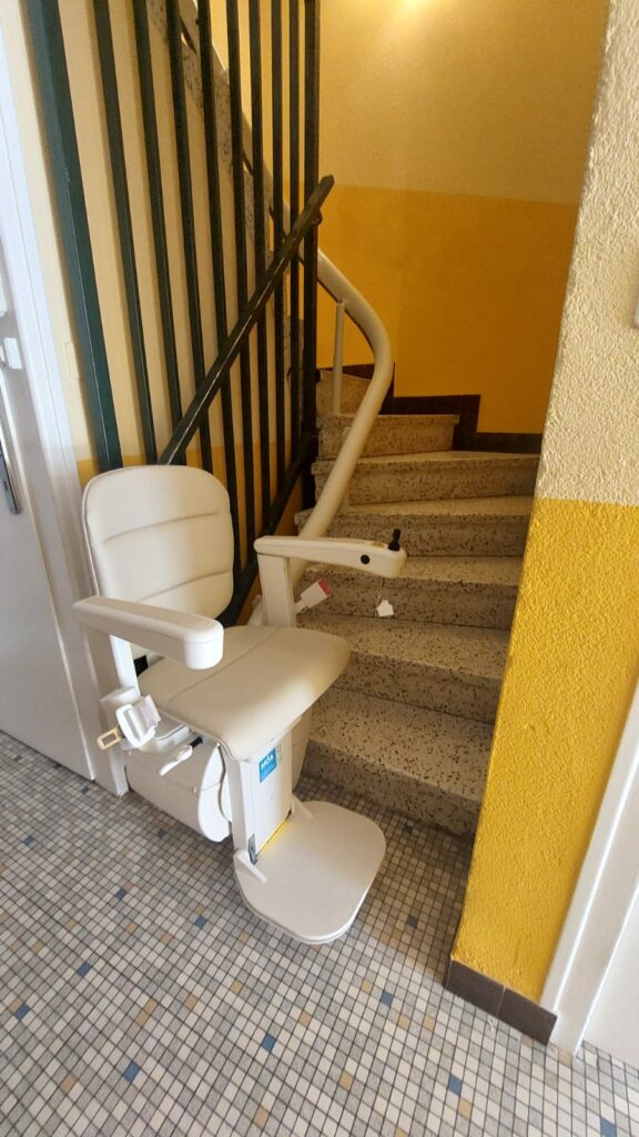 Monte-escalier avec siège beige en bas d'un escalier avec garde-corps métallique noir