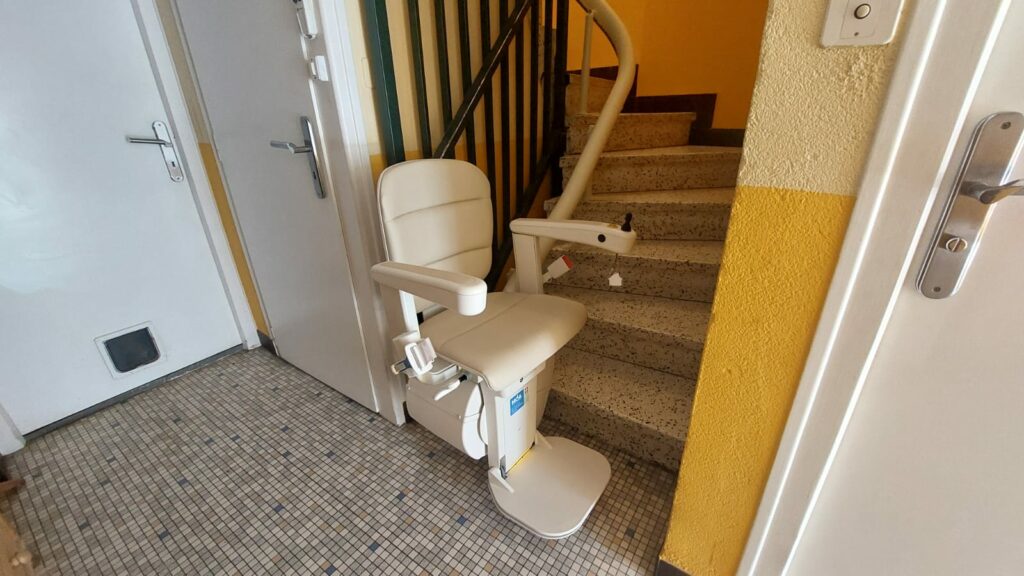 Monte-escalier avec siège beige en bas d'un escalier avec garde-corps métallique noir