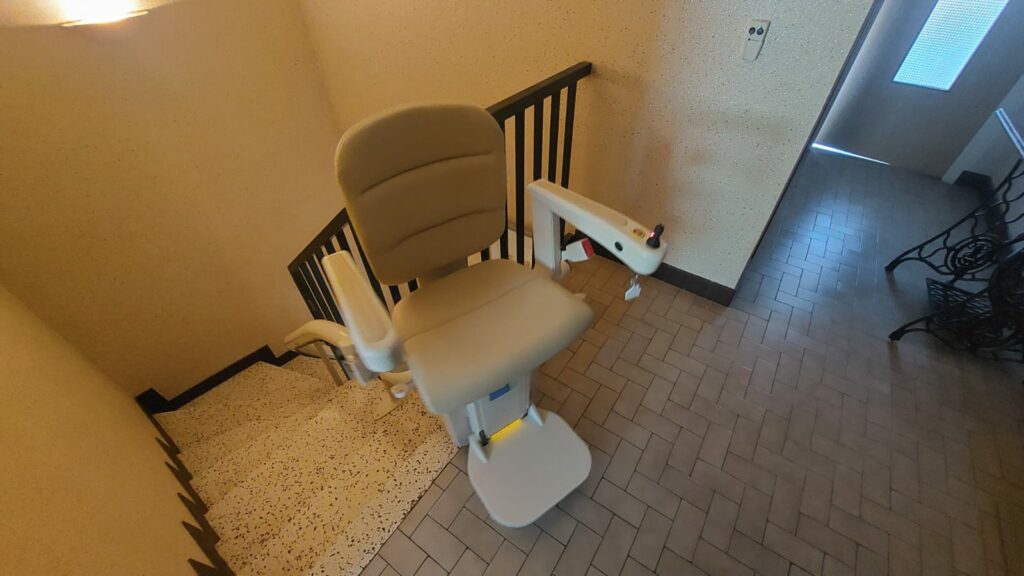 Monte-escalier avec siège beige en bas d'un escalier avec garde-corps métallique noir