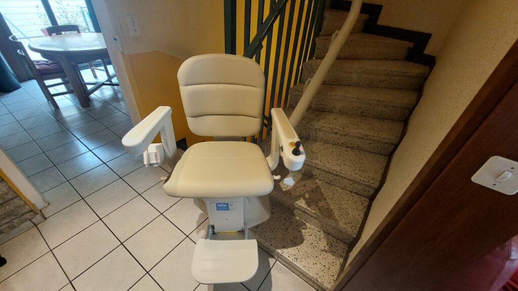 Monte-escalier avec siège beige en bas d'un escalier avec garde-corps métallique noir