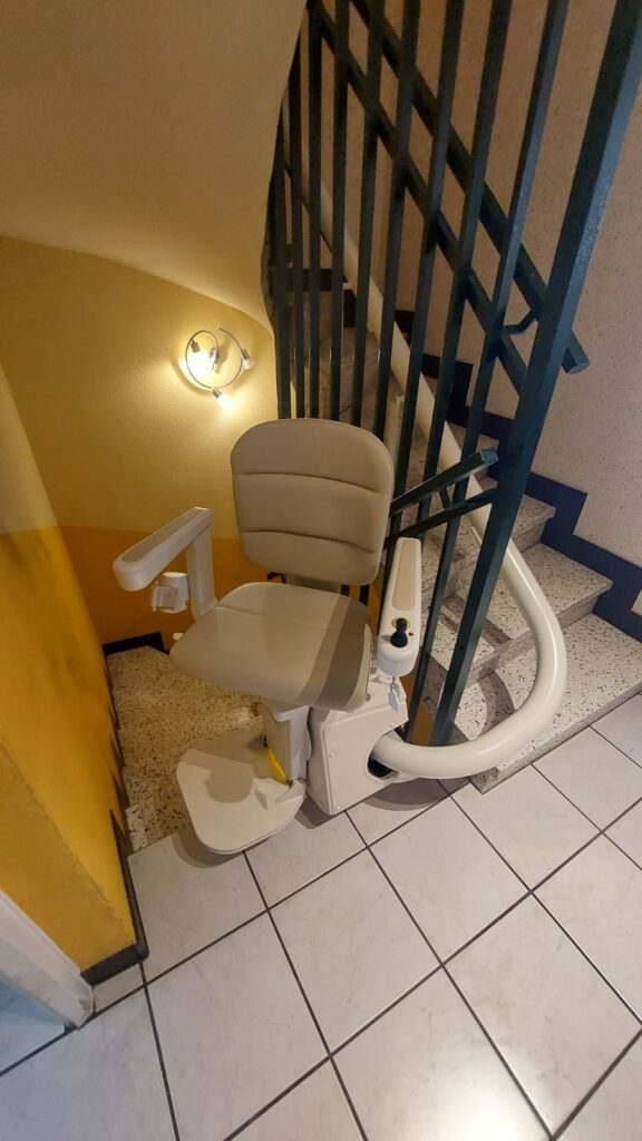 Monte-escalier avec siège beige en bas d'un escalier avec garde-corps métallique noir