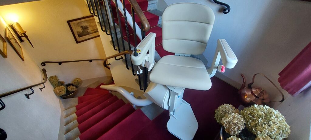 Monte-escalier avec siège beige installé sur escalier courbe avec moquette rouge