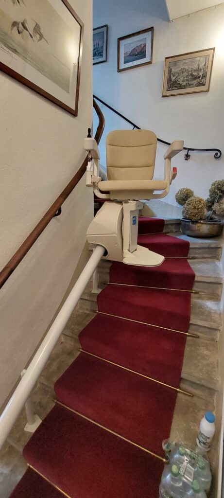 Monte-escalier avec siège beige installé sur escalier courbe avec moquette rouge