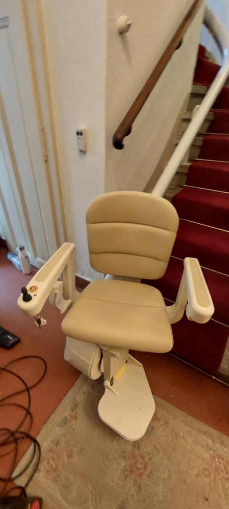 Monte-escalier avec siège beige installé sur escalier courbe avec moquette rouge