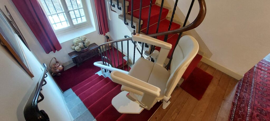 Monte-escalier avec siège beige installé sur escalier courbe avec moquette rouge