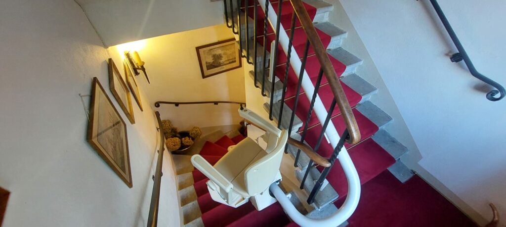 Monte-escalier avec siège beige installé sur escalier courbe avec moquette rouge