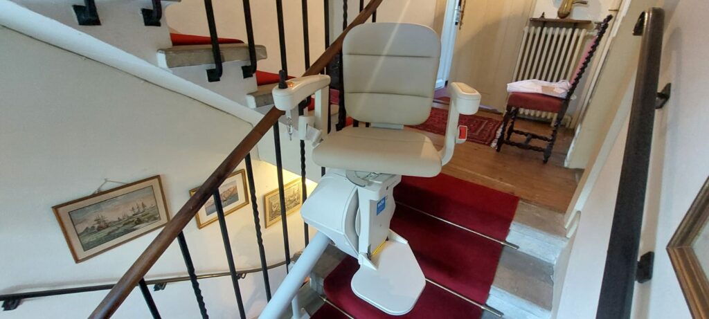 Monte-escalier avec siège beige installé sur escalier courbe avec moquette rouge